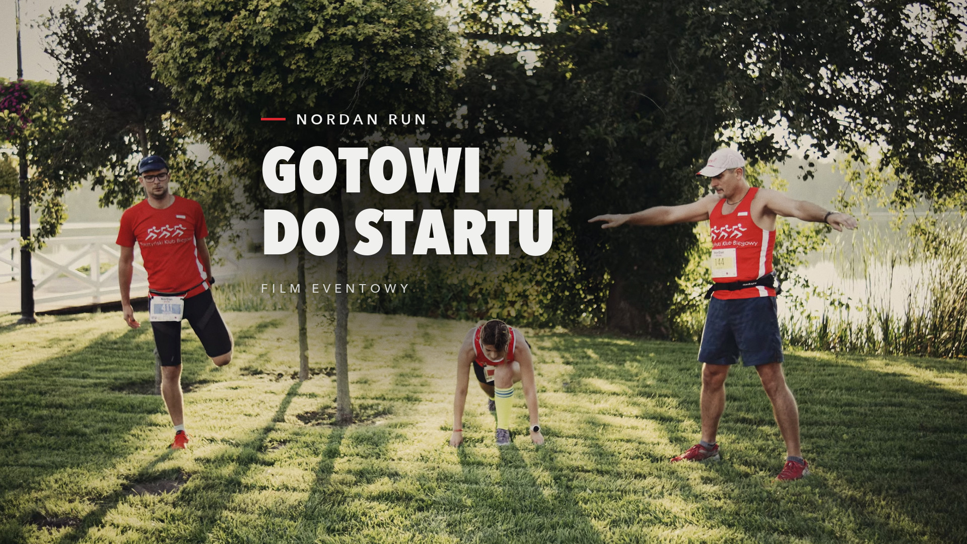 Biegacze w czerwonych koszulkach klubu biegowego rozgrzewają się na trawie przed startem Nordan RUN, kadr z filmu eventowego 302 Studio
